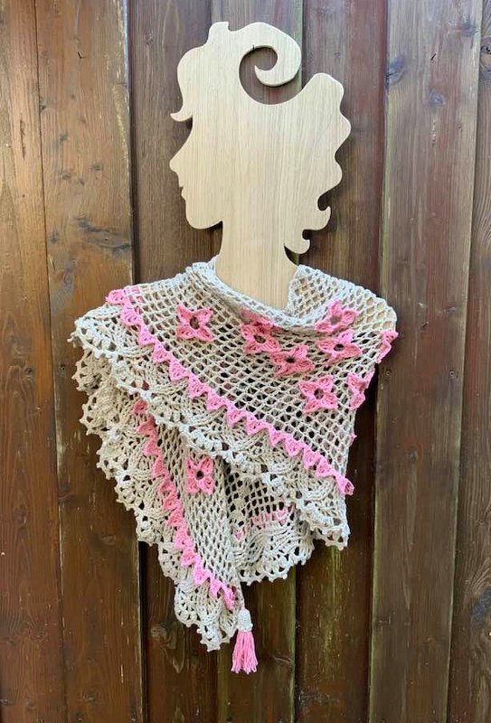 Gehäkeltes Dreieckstuch in Beige mit rosa Blütenapplikationen und Quaste, drapiert auf Holzfigur