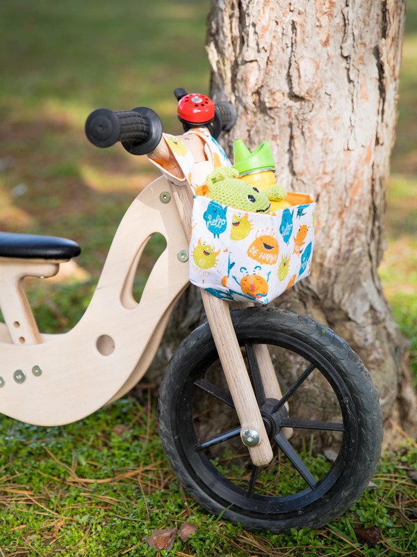 Laufrad mit praktischer Lenker-Tasche aus gemustertem Stoff, befüllt mit Becher und Kuscheltier