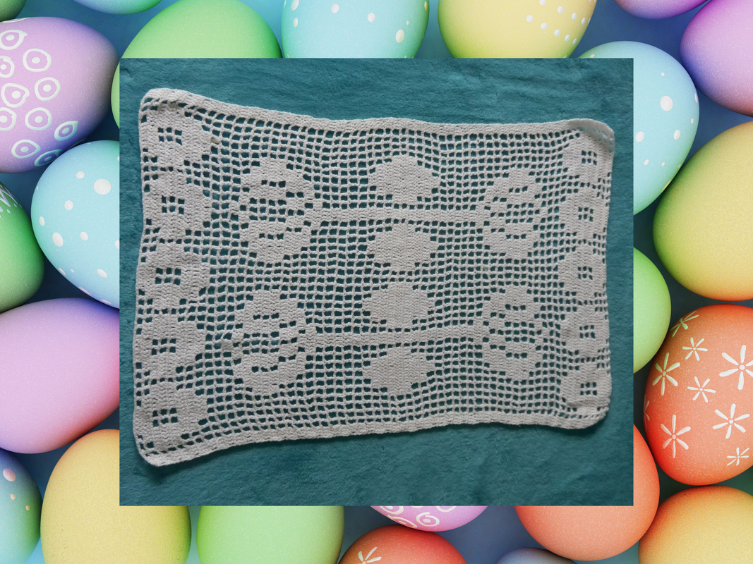 Rechteckiges weißes Filetdeckchen mit klarem Kästchenraster und Blütenmotiven auf türkisem Untergrund