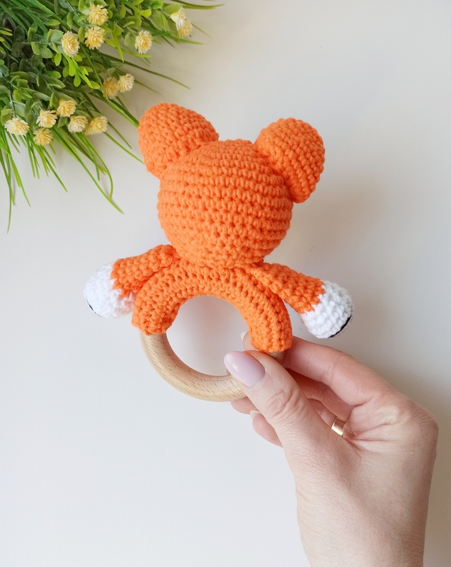 Close-up of a wooden ring teether with an orange crocheted animal rattle held by a hand