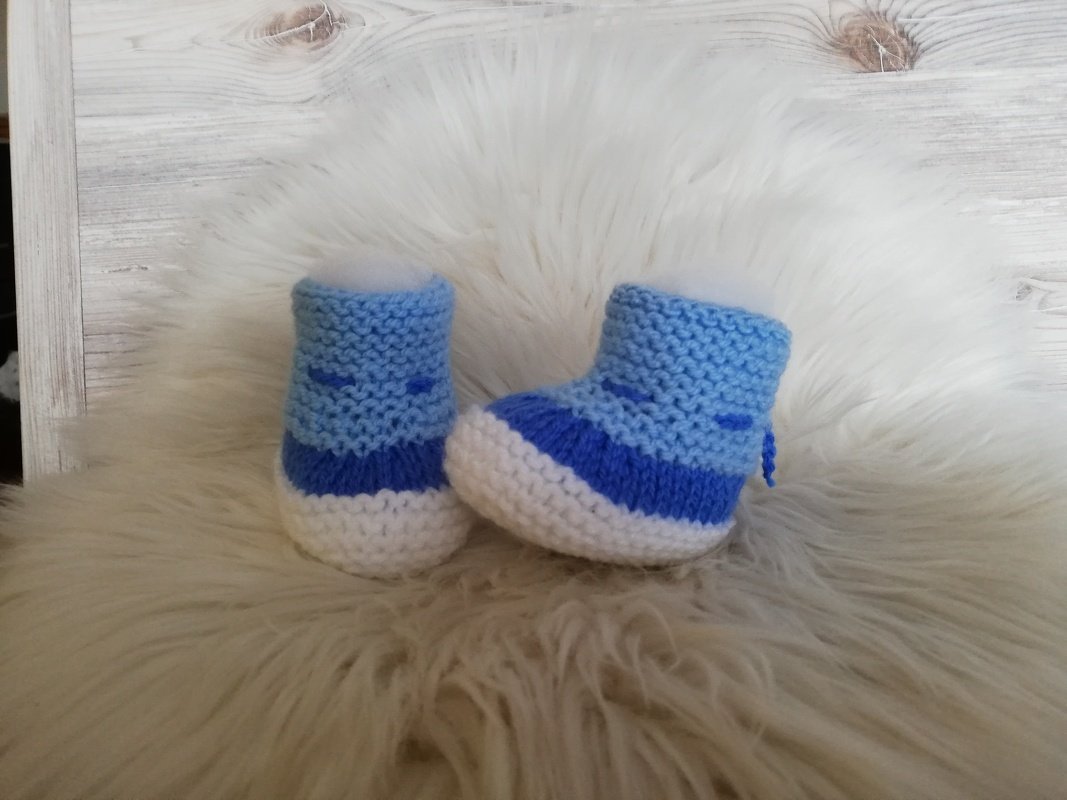 Gestrickte hellblaue Babyschuhe mit weißer Sohle auf hellem Fell