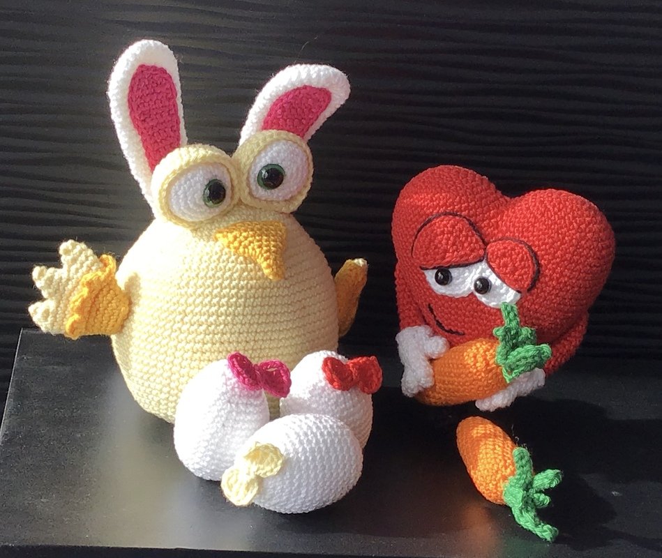 Gehäkeltes gelbes Küken mit Hasenohren, rotes Herz-Amigurumi mit Karotte und drei weiße Amigurumi-Eier.