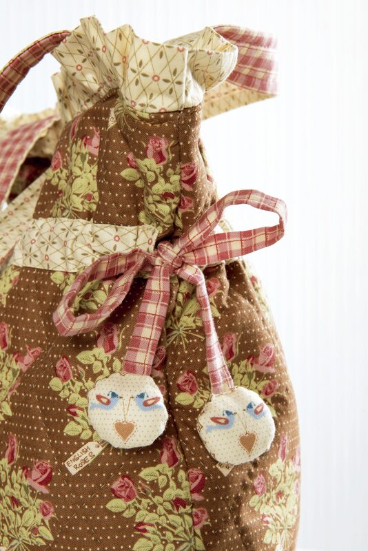 Brauner Stoffbeutel mit Blumenmuster, Kordelzug und runden Stoffanhängern