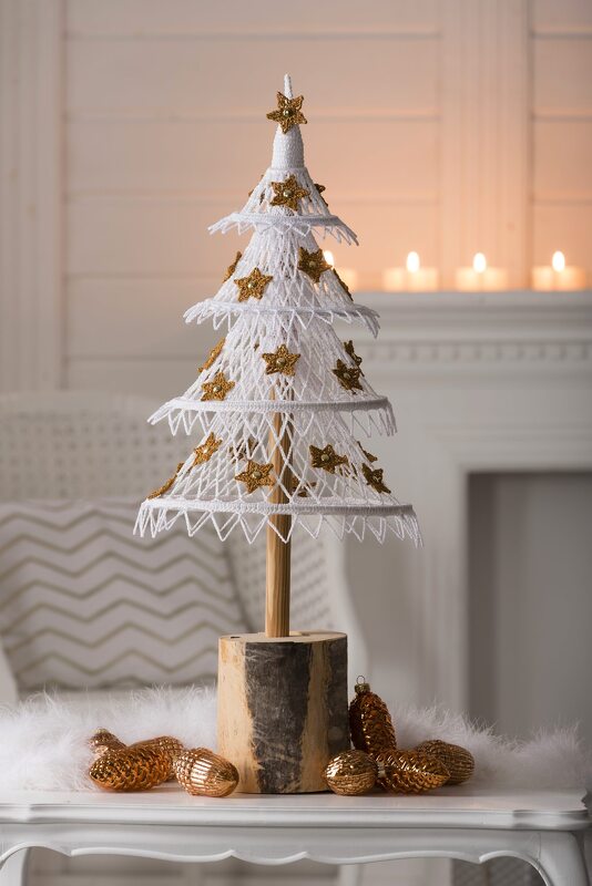 Weiß gehäkelter mehrstufiger Weihnachtsbaum mit goldenen Sternen auf Holzsockel, umgeben von goldenen Kugeln
