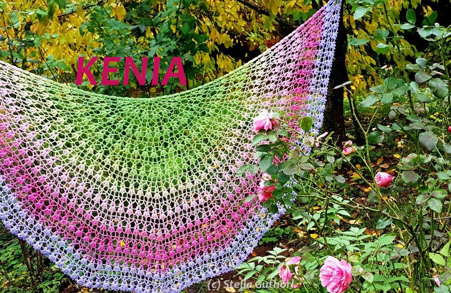 Halbrundes gehäkeltes Tuch mit Farbverlauf in Grün, Pink und Lila, drapiert an Rosen im Garten