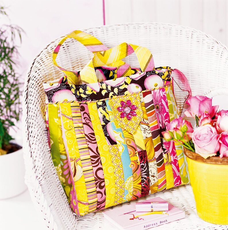 Bunte Streifen-Patchwork-Tasche in Gelb und Pink auf weißem Korbstuhl mit Blumenapplikation