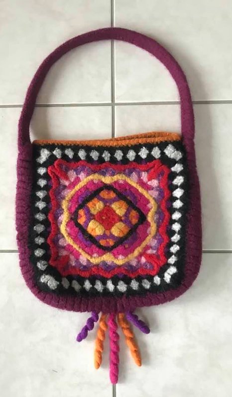 Bunte gehäkelfilzte Tasche mit zentralem Granny‑Square‑Muster und Quasten