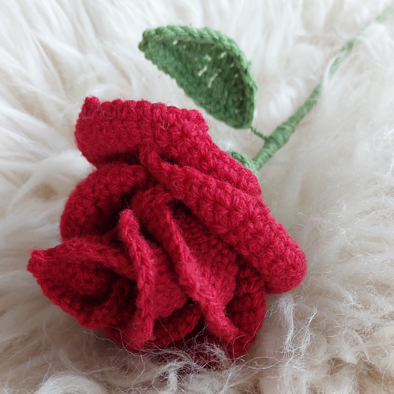 Rote gehäkelte Rose mit grünem Stiel und Blatt auf hellem Fell