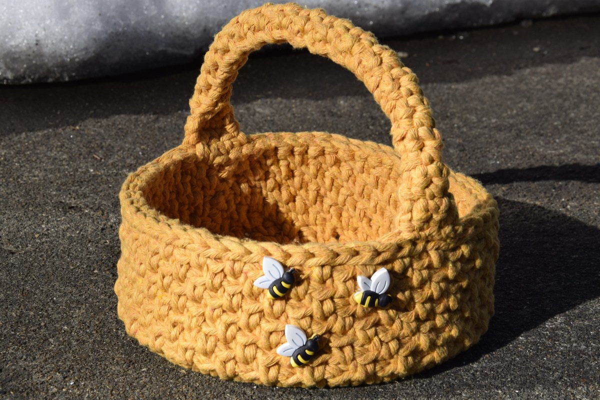 Gehäkelter ockerfarbener Korb mit Henkel und drei Bienenknöpfen