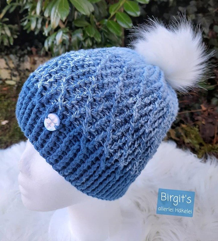 Hellblau melierte gehäkelte Mütze mit weißem Bommel und kleinem Zierknopf auf einem Mannequinkopf