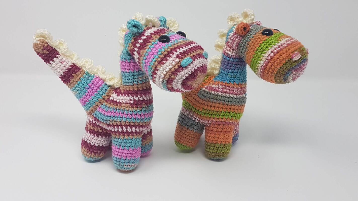 Zwei bunt gestreifte gehäkelte Amigurumi-Dinosaurier mit heller Rücken-Zackenreihe