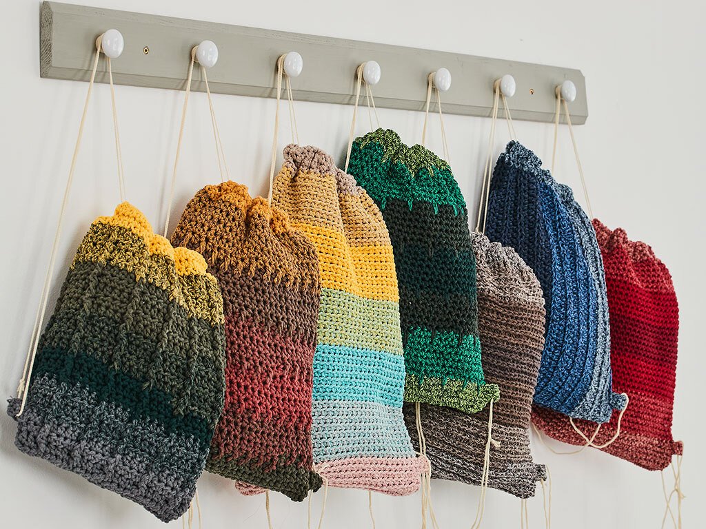 Bunte gehäkelte Turnbeutel in Streifen- und Farbverläufen an einer Hakenleiste