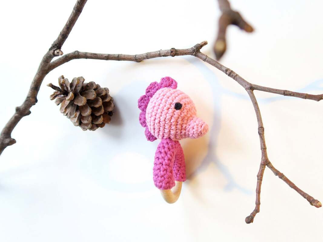Rosa gehäkeltes Seepferdchen an Holzring neben Zweigen und Zapfen