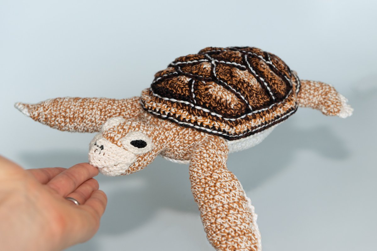 Close-up of crochet sea turtle amigurumi showing layered shell, contrast outlines, and a hand for scale