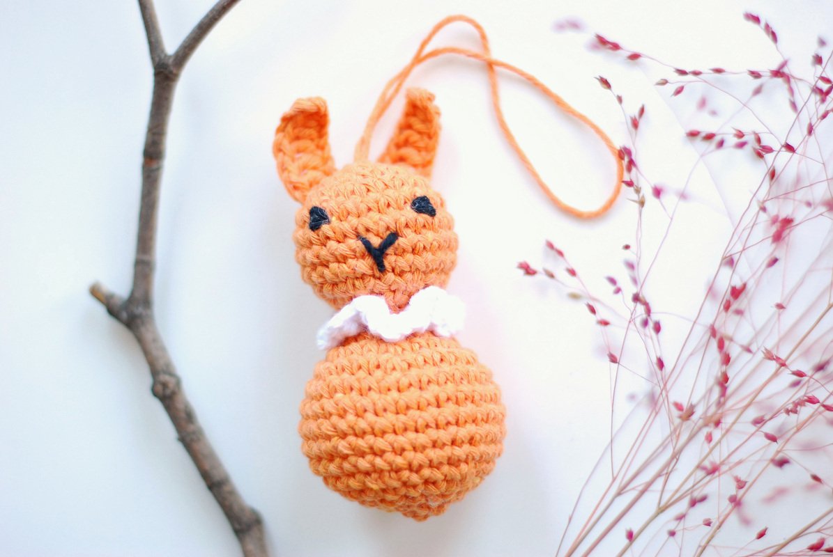 Gehäkelte orangefarbene Hasenrassel mit weißem Kragen und Aufhängeschlaufe
