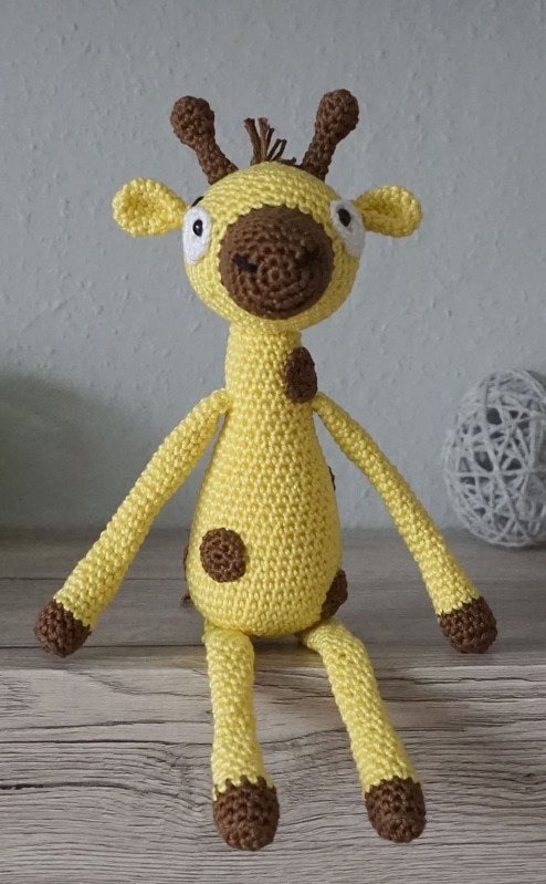 Gelb-braune gehäkelte Amigurumi-Giraffe sitzend auf Holzoberfläche