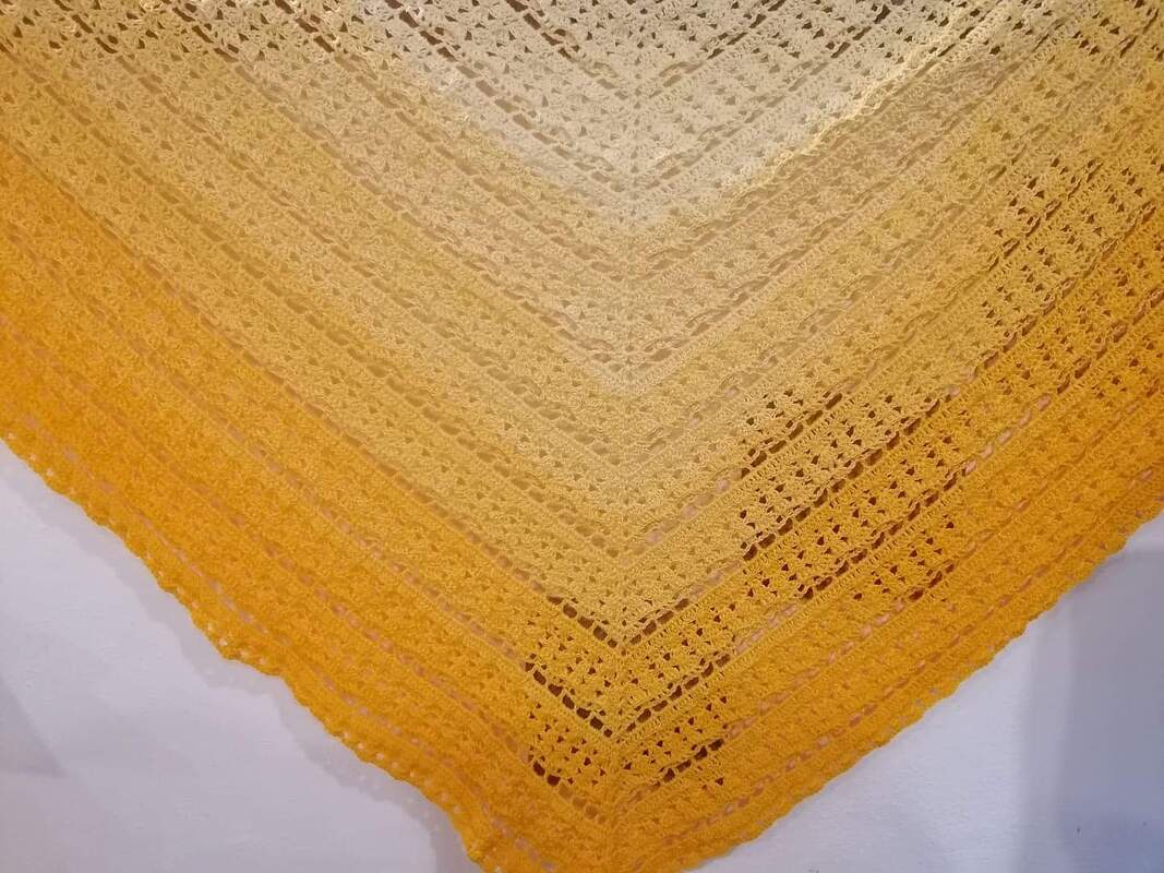 Nahaufnahme eines gehäkelten Dreieckstuchs in Gelb- und Orangetönen mit Lochmuster.