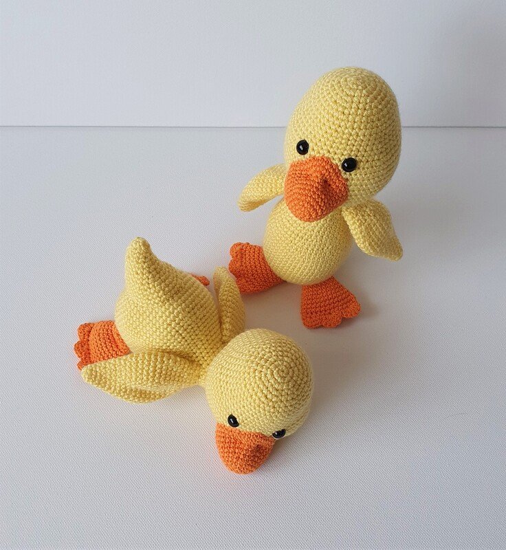 Zwei gelbe Amigurumi Entenküken mit orangefarbenem Schnabel und Füßen auf hellem Hintergrund