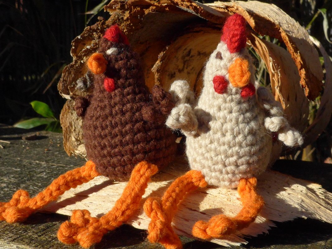 Zwei kleine gehäkelte Hühner-Amigurumi mit gedrehten orangen Beinen
