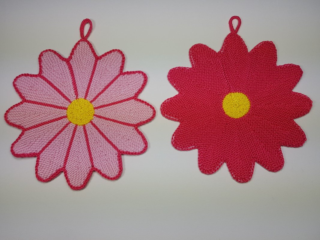 Zwei gestrickte Blumentopflappen in Rosa und Dunkelrosa mit gelber Mitte und Aufhängeschlaufe.