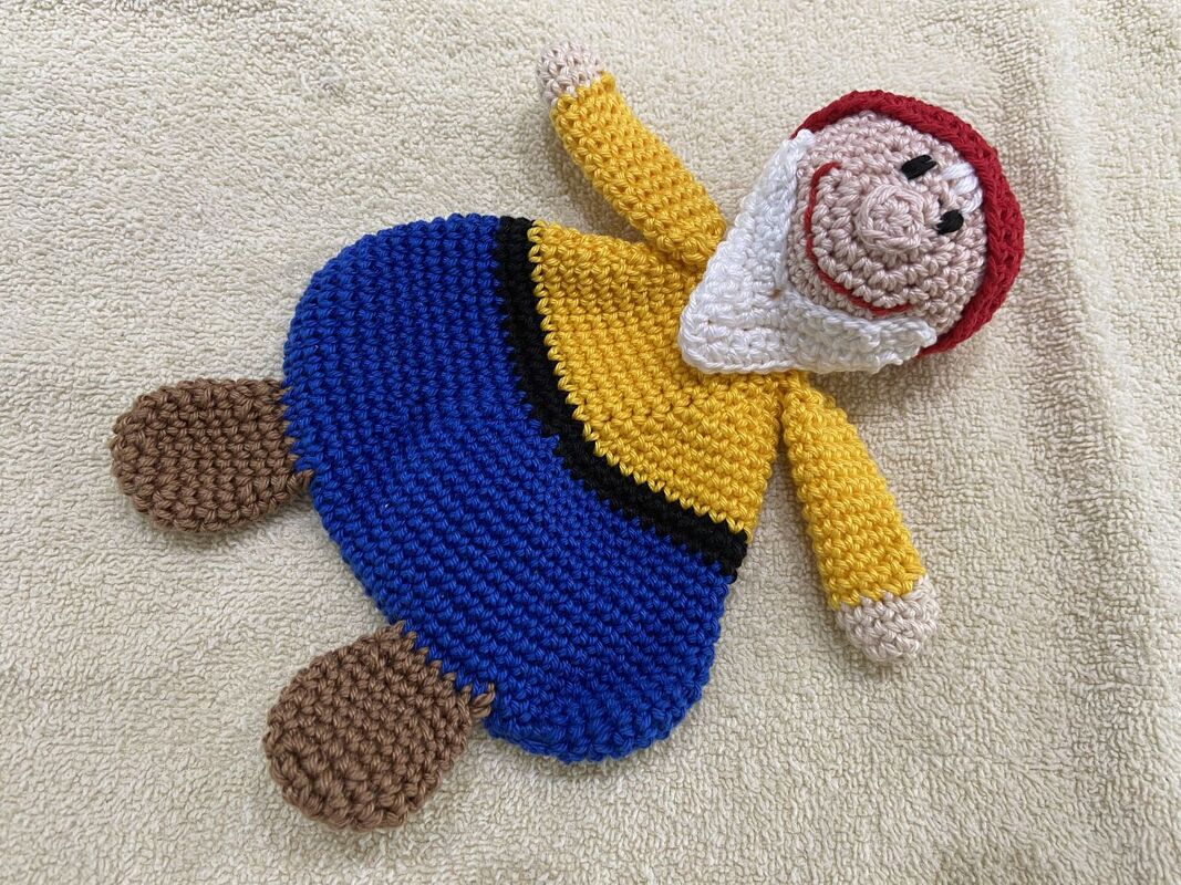 Gehäkeltes Schmusetuch Gnom mit roter Mütze, weißem Bart und blauem Unterteil, liegend auf hellem Tuch