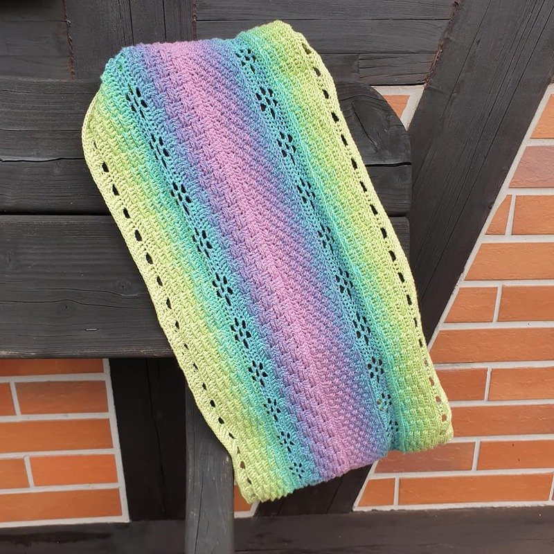 Gehäkelter Loop in Pastellfarben (Gelb, Grün, Blau, Rosa) mit Lochblütenmuster, über eine Holzleiste gelegt