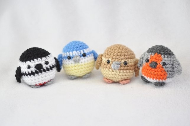 Vier gehäkelte Amigurumi-Vögel: schwarz-weiß, Blaumeise, Spatz, Rotkehlchen.