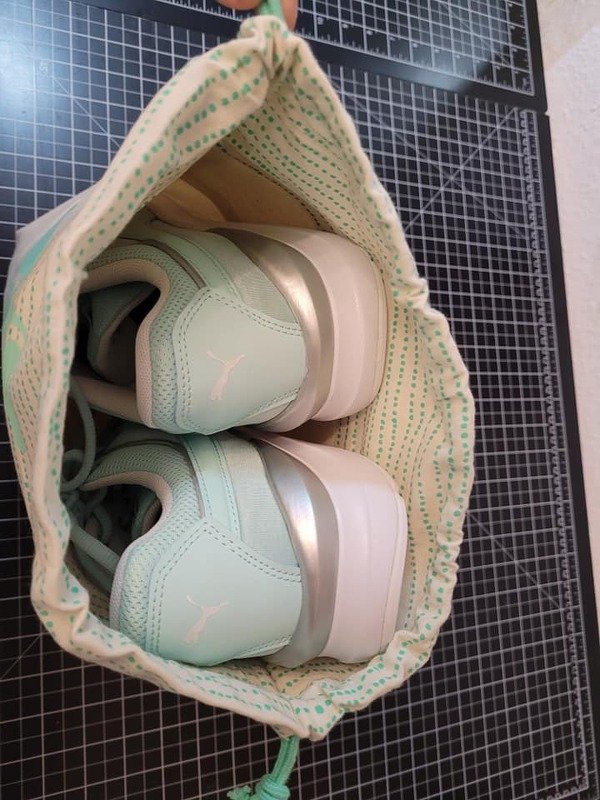 Zwei mintgrüne Sportschuhe in einem beigen Stoffbeutel mit grünen Punkten auf einer schwarzen Schneidematte.
