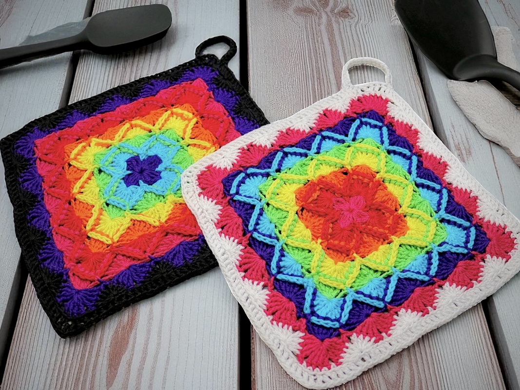Zwei gehäkelte Topflappen in Regenbogenfarben mit sternförmigem Muster und Aufhängeschlaufen auf Holzuntergrund