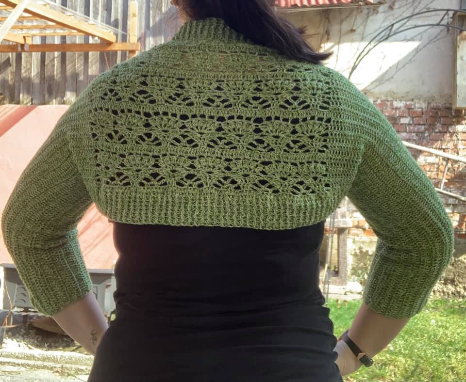 Rückansicht: grüner, gehäkelter Bolero mit offenem Lochmuster und gerippten Bündchen.