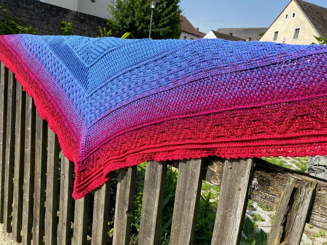 Gehäkeltes Dreieckstuch mit Farbverlauf von Blau bis Rot, auf einem Holzzaun drapiert