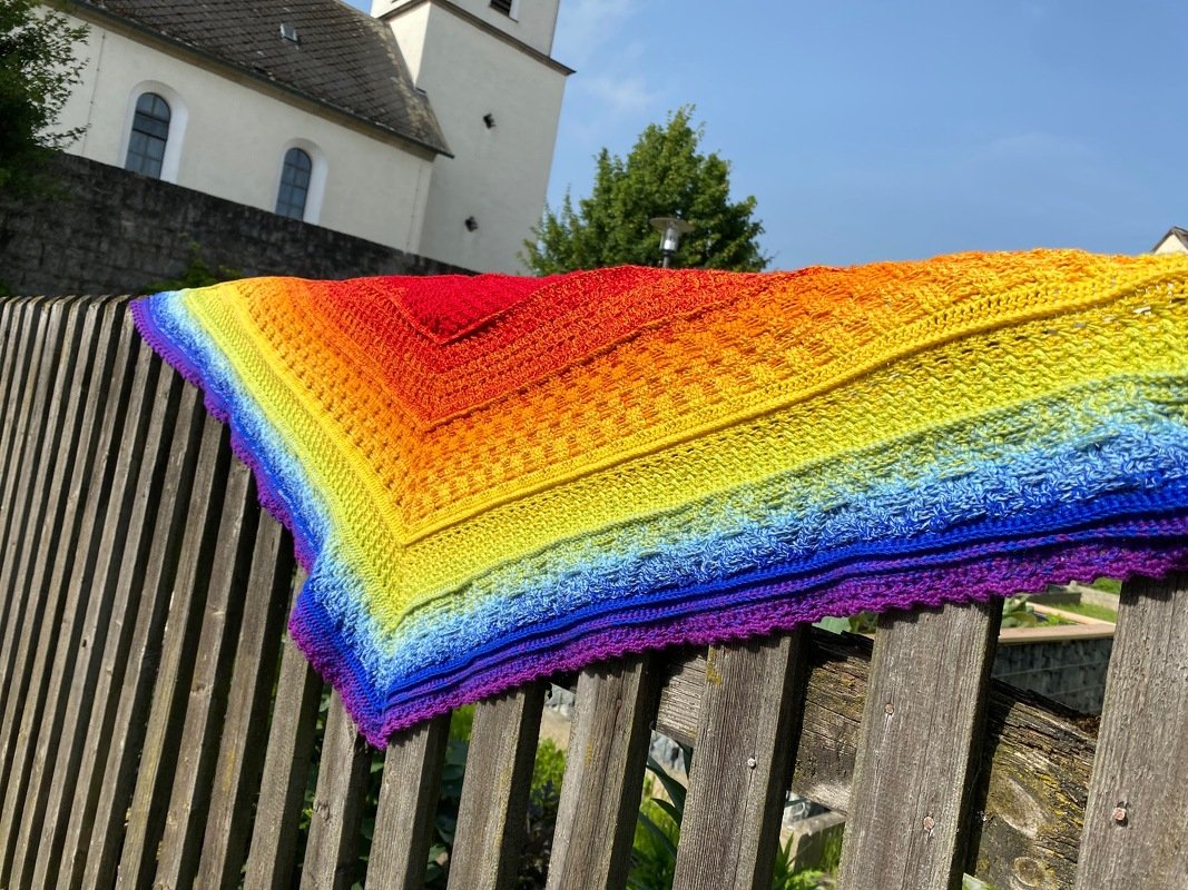 Gehäkeltes Dreieckstuch mit Regenbogen-Farbverlauf auf Holzzaun
