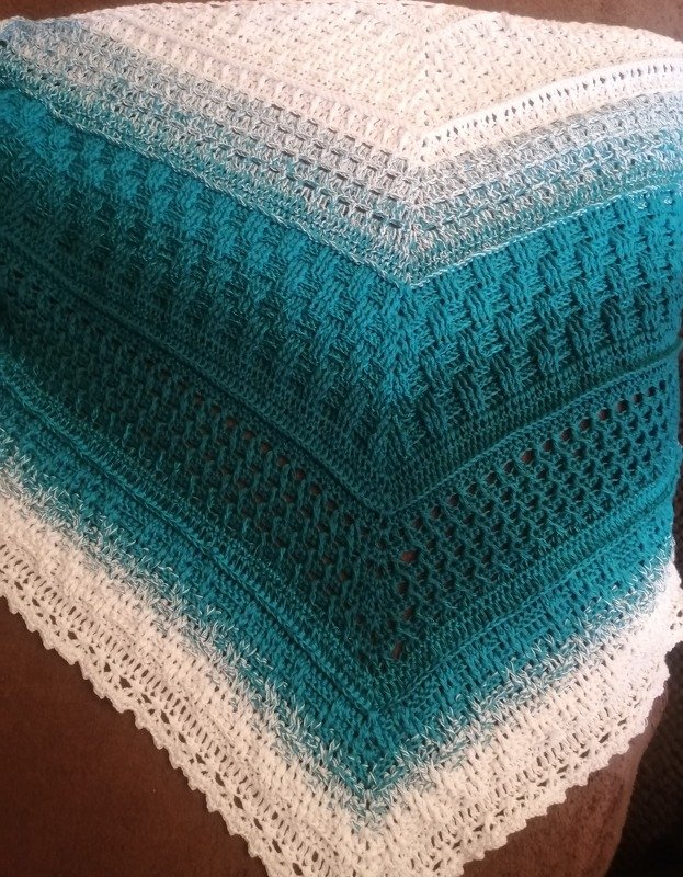 Nahaufnahme eines gehäkelten Dreieckstuchs mit Türkis‑Weiß‑Verlauf und verschiedenen Musterstreifen