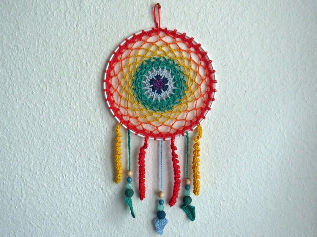 Bunter gehäkelter runder Wandbehang mit konzentrischem Muster, Holzperlen und hängenden Quasten an weißer Wand