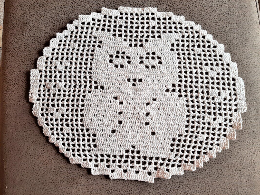 Weißes rundes Häkeldeckchen mit Eulenmotiv auf braunem Stoff