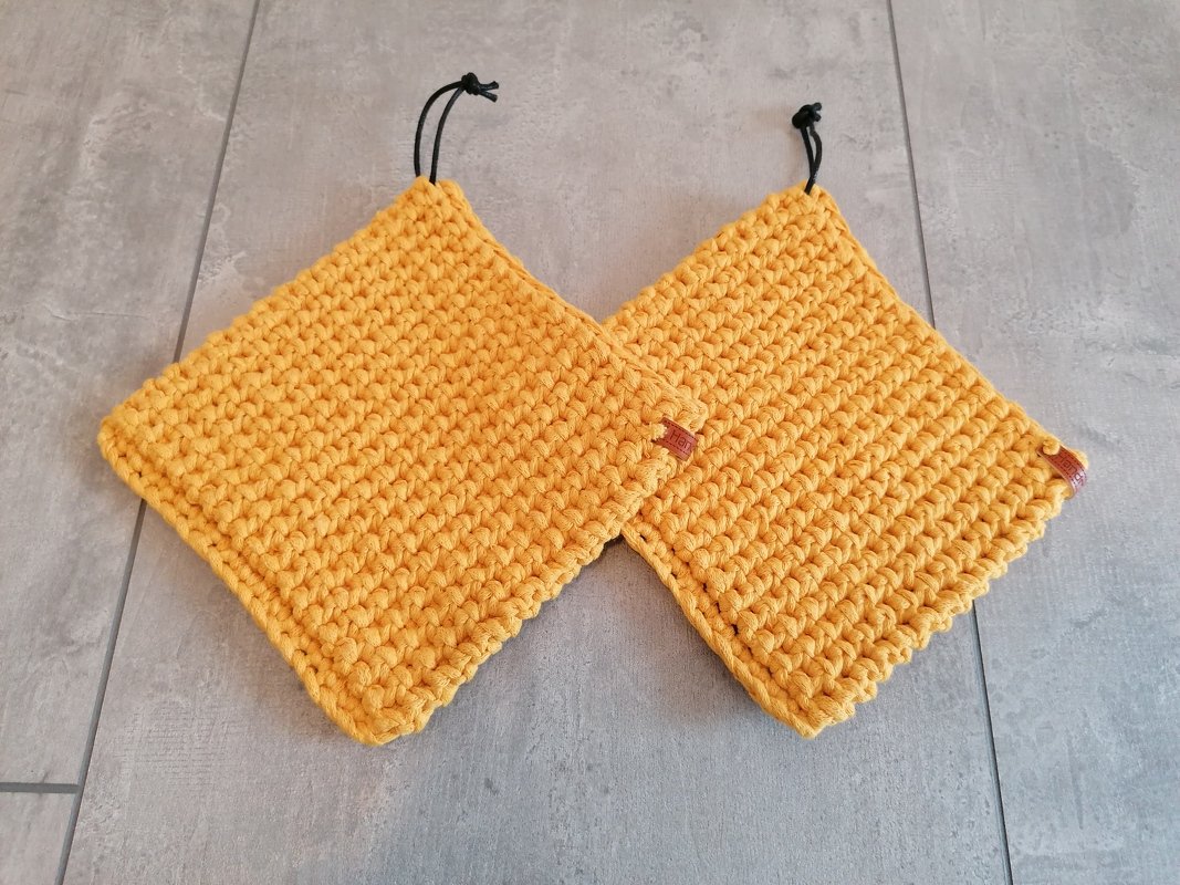 Zwei gehäkelte quadratische Topflappen in Senfgelb mit schwarzen Aufhängeschlaufen