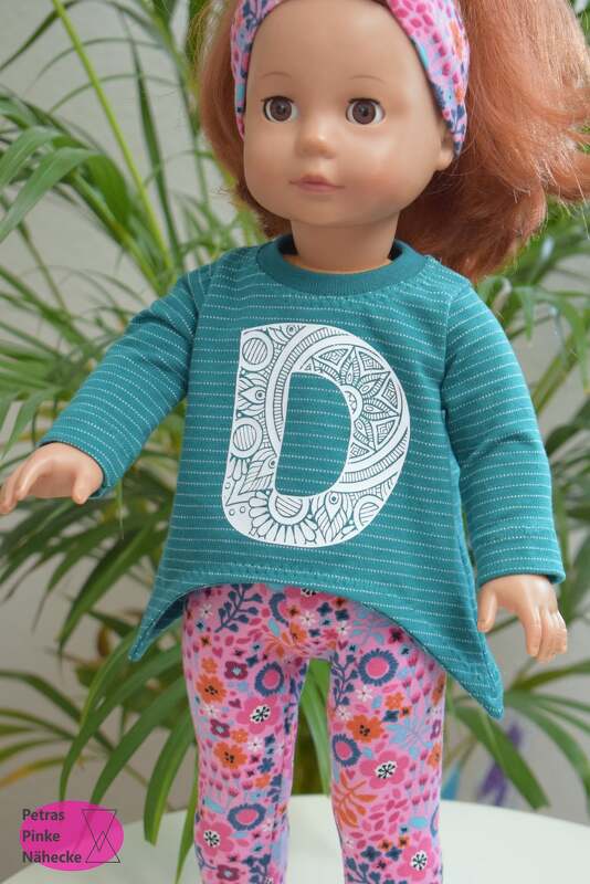 Puppe in türkisfarbenem Langarmshirt mit gemustertem Buchstaben D und pinken Blumenleggings.