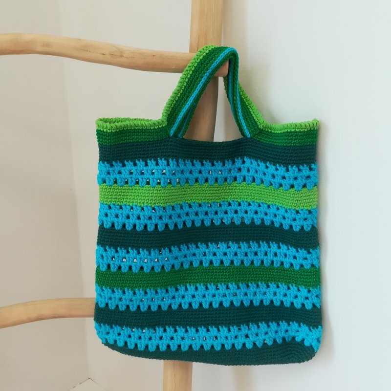 Gehäkelte Henkeltasche in Blau und Grün mit Streifenmuster, an einer Holzleiter hängend