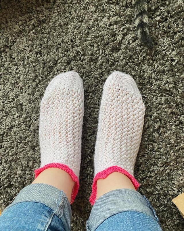 Füße mit hellen gestrickten Knöchelsocken mit pinker gewellter Kante auf grünem Teppich