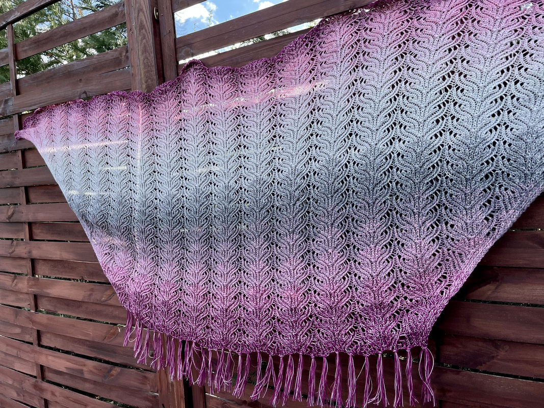 Gestricktes Lacetuch in Pink bis Grau mit Blattmuster und Fransen an einem Holzzaun