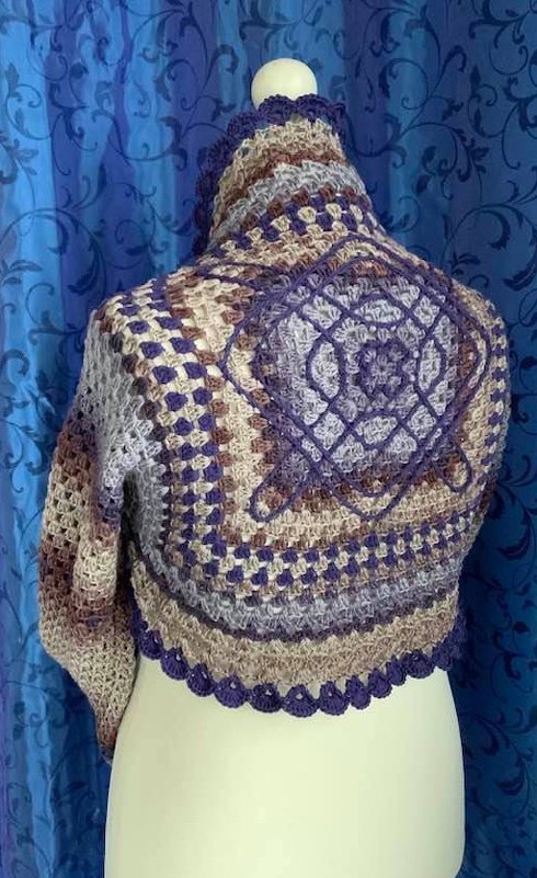 Rückenansicht eines gehäkelten Damen-Boleros mit großem Granny-Quadrat in Lila und Beige und Muschelrand