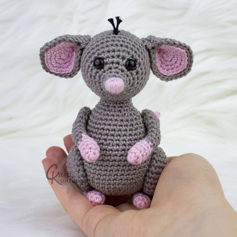 Handgehäkelte graue Amigurumi‑Maus mit rosa Ohren und Nase, gehalten in einer Hand