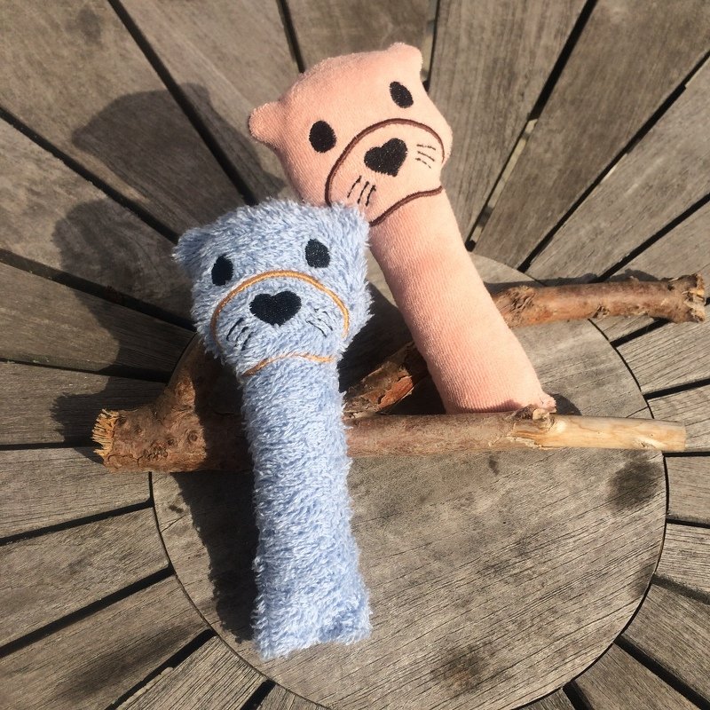 Zwei Stabrasseln mit bestickten Bärengesichtern nebeneinander auf einem runden Holztisch