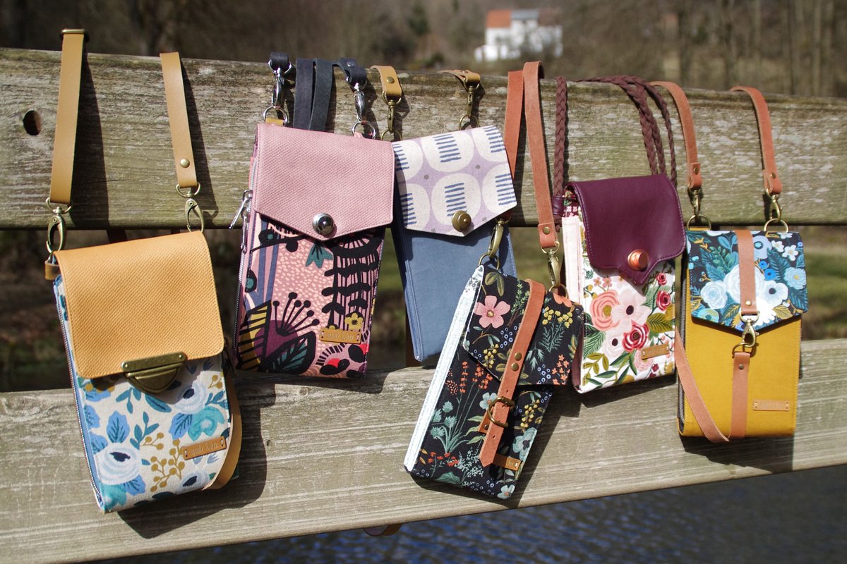 Mehrere kleine Stofftaschen in bunten Mustern an einem Holzgeländer.