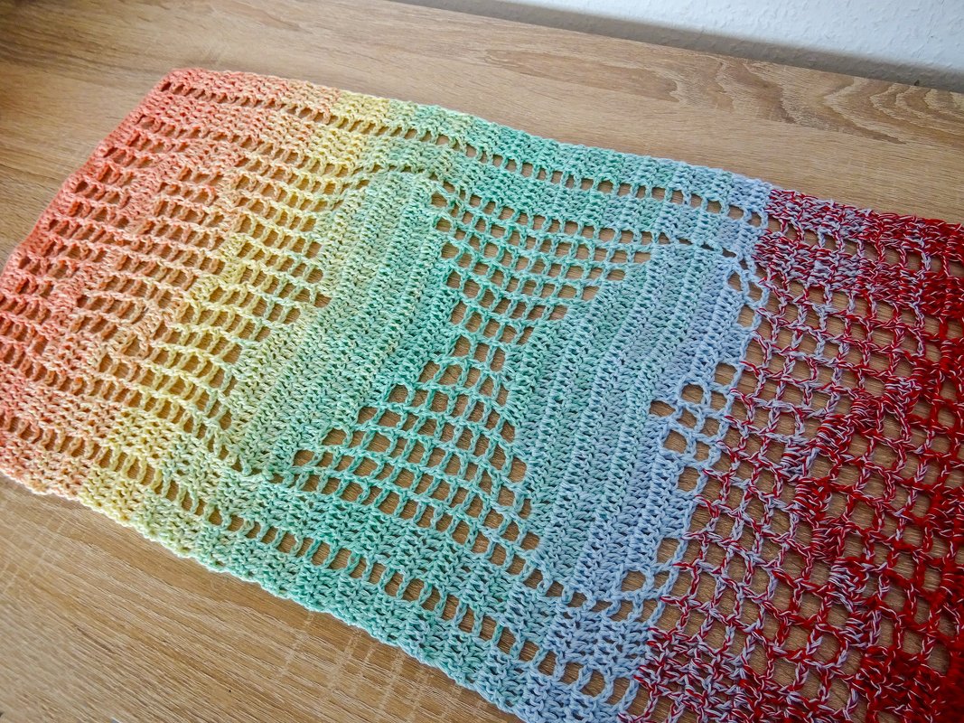 Handgehäkelter Tischläufer in Regenbogenfarben mit durchbrochenem Herzmuster auf hellem Holztisch