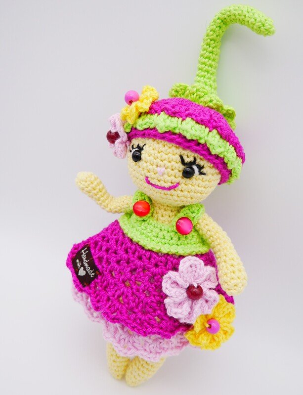 Handgehäkelte Amigurumi-Puppe mit spitzem Hut, pink-grünem Kleid und Blumenapplikationen.