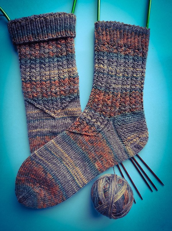 Paar handgestrickter mehrfarbiger Damensocken mit Knäuel und Nadelspiel auf blauem Hintergrund