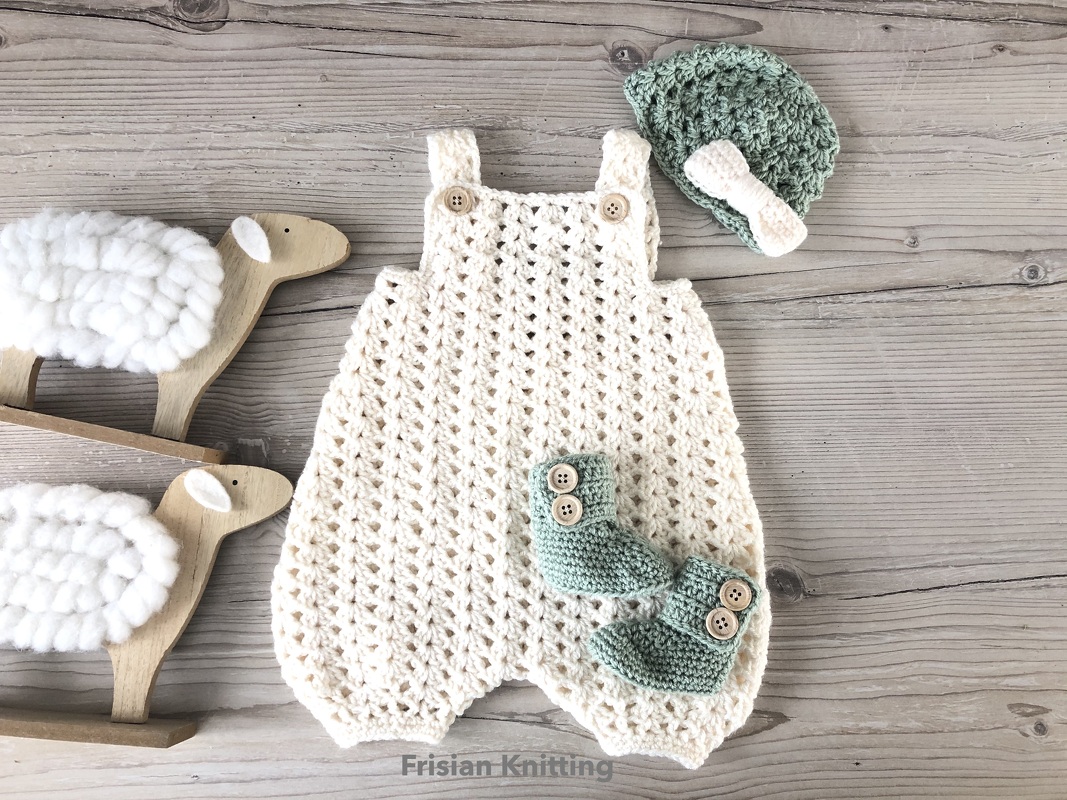 Gehäkelter beigefarbener Strampler, mintgrüne Mütze mit Schleife und mintgrüne Babyschühchen auf hellem Holzhintergrund neben Holzschafen.