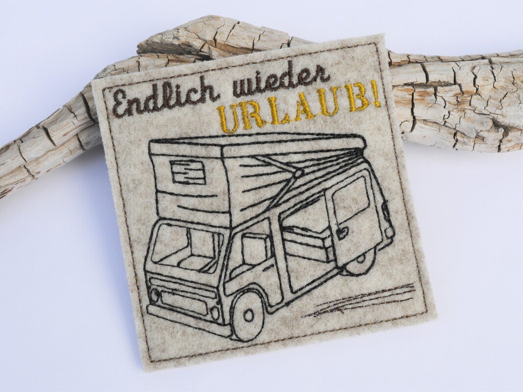 Beiger quadratischer Tassenteppich aus Filz mit gesticktem Camper und dem Schriftzug „Endlich wieder URLAUB!“.