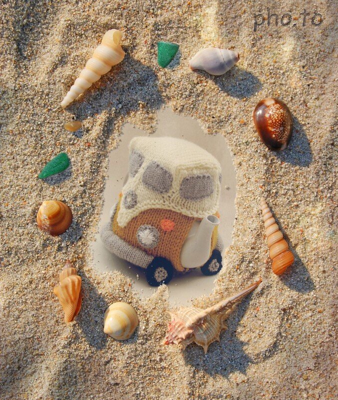 Cream-and-brown knitted camper van toy in sand surrounded by seashells and sea glass